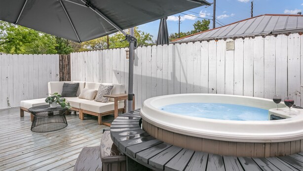 A wooden deck with a hot tub, a white outdoor sofa, and a table with a plant.