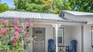 A house with a grey door, two blue Adirondack chairs, a small table, and a flower bush in front. - Main Street Retreat Almost Heaven Suite | King Bed | Shared Hot Tub/Pool (Fredericksburg)
