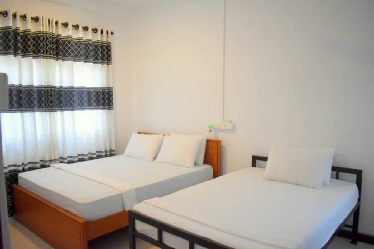 A hotel room with two single beds, a wooden headboard, a nightstand, a lamp, and a window with curtains.