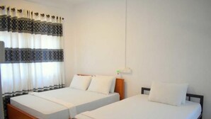 Ein Hotelzimmer mit zwei Einzelbetten, einem Holz-Kopfstück, weißer Bettwäsche und einem Fenster mit durchsichtigen Vorhängen.