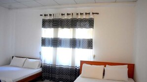 Ein Zimmer mit zwei Betten, einem Fenster mit gemusterten Vorhängen und einer schlichten weißen Wand.