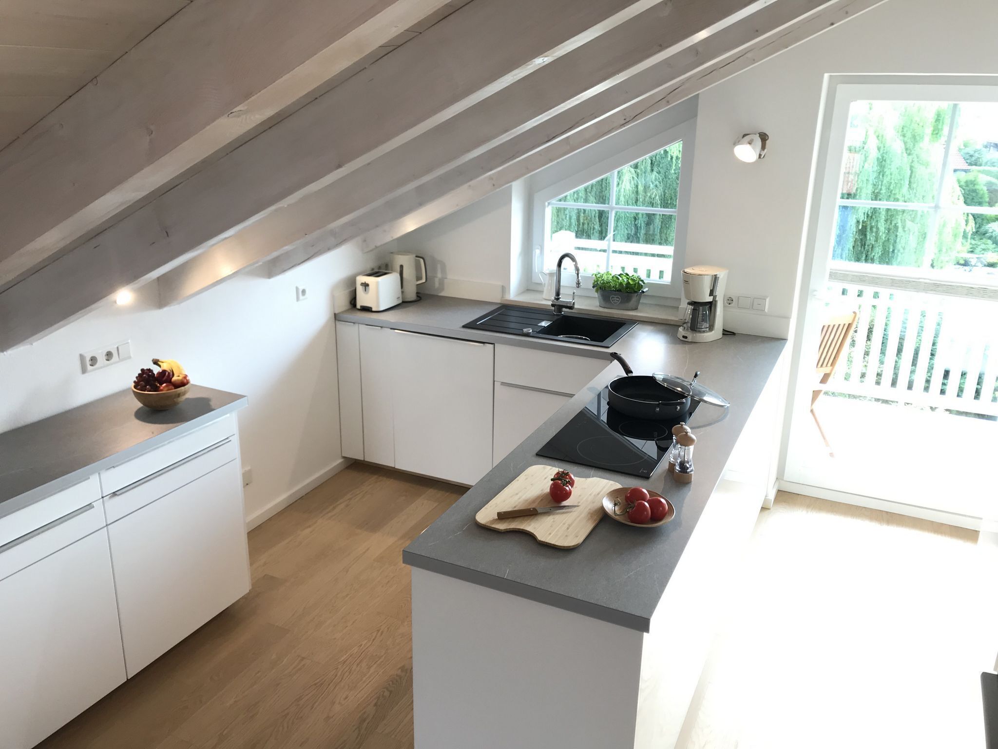 Een moderne keuken met witte kasten, een houten plafond en een groot raam dat voor natuurlijk licht zorgt.