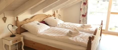 A bedroom with a wooden bed, white bedding, a nightstand with a lamp, and a window with curtains.