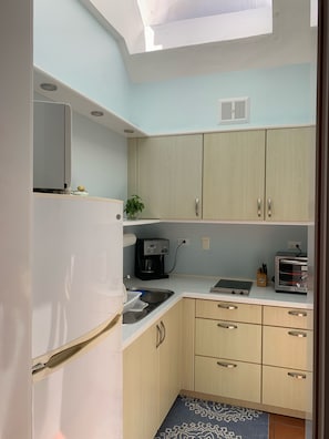 Compact kitchen with modern design, featuring a refrigerator, oven, sink, and coffee maker.