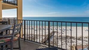 A balcony with a view of a beach, featuring a wooden table and chairs, and a railing. - ~ 3 Bedroom Condo ~ Book Now for Great Rates! (Orange Beach)