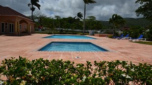 A swimming pool with tiled flooring, surrounded by palm trees and lounge chairs. - The Monet Place (Ocho Rios)