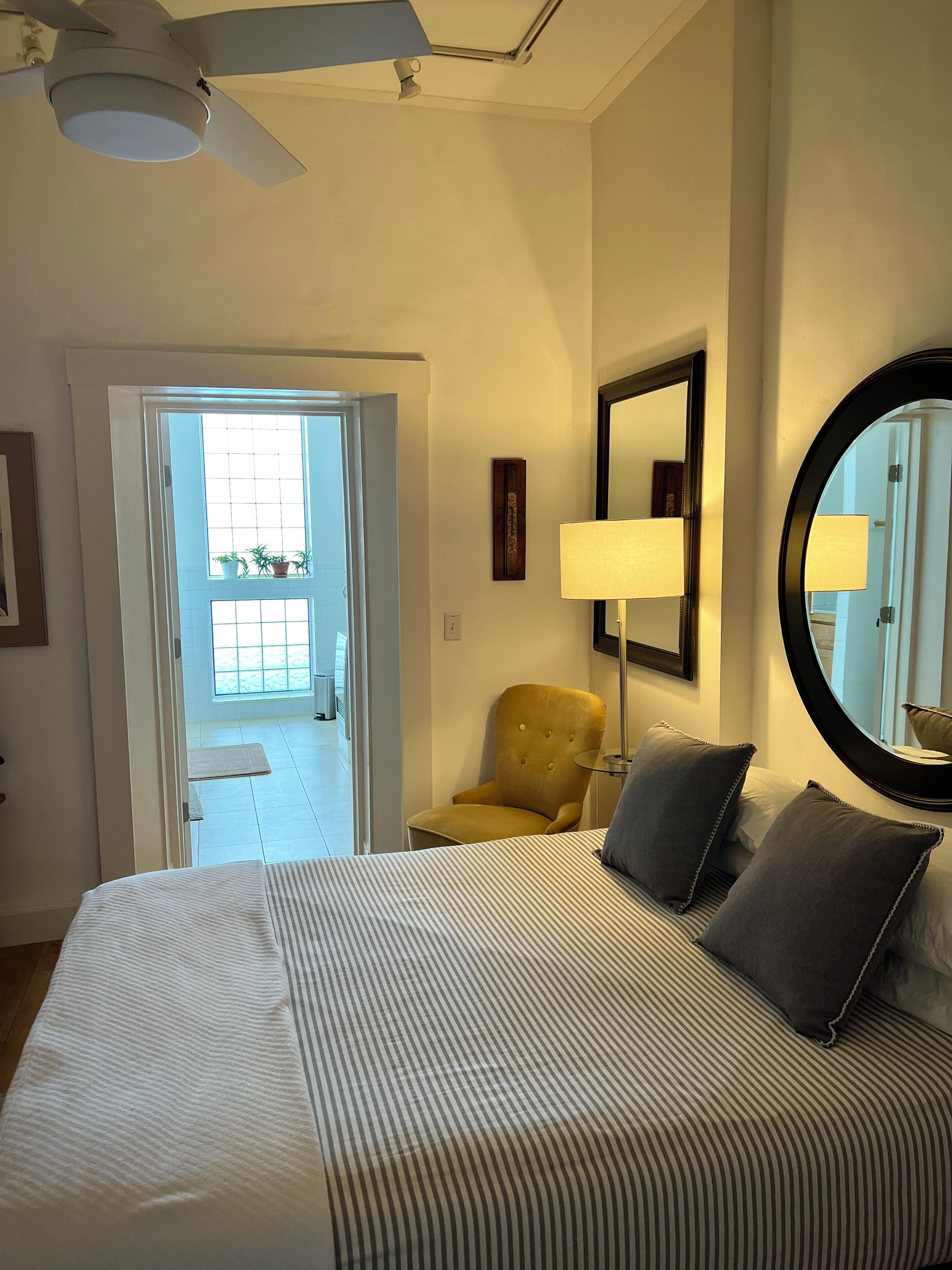 A hotel room with a bed, a chair, a lamp, a mirror, and a door leading to a balcony.