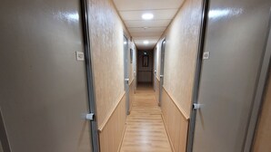 Un pasillo estrecho con suelo de madera y puertas metálicas, cada una con un número.
