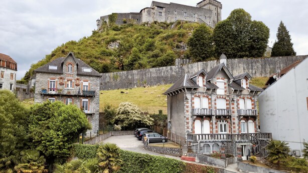 Un edificio histórico de piedra con un balcón y vistas a un castillo en una colina.