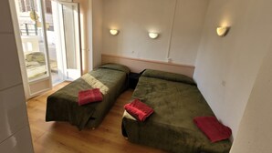 Una habitación con dos camas individuales, piso de madera, una puerta corrediza de vidrio que da al exterior y dos lámparas fijadas a la pared.