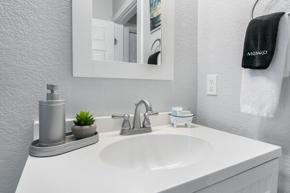 A modern bathroom with a white sink, a large mirror, a faucet, a soap dish, and a towel rack with a black towel.