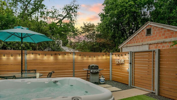Een achtertuin met een jacuzzi, houten omheining en een barbecue.