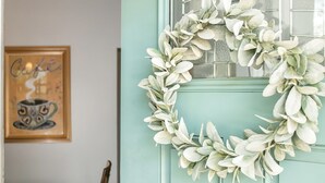 Een blauwgroene deur met een geëtste ruit, een witte krans en een lijst met een foto aan de muur.