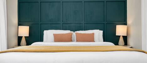 Una habitación de hotel con una cama grande, ropa de cama blanca, dos almohadas estampadas y dos lámparas de noche.