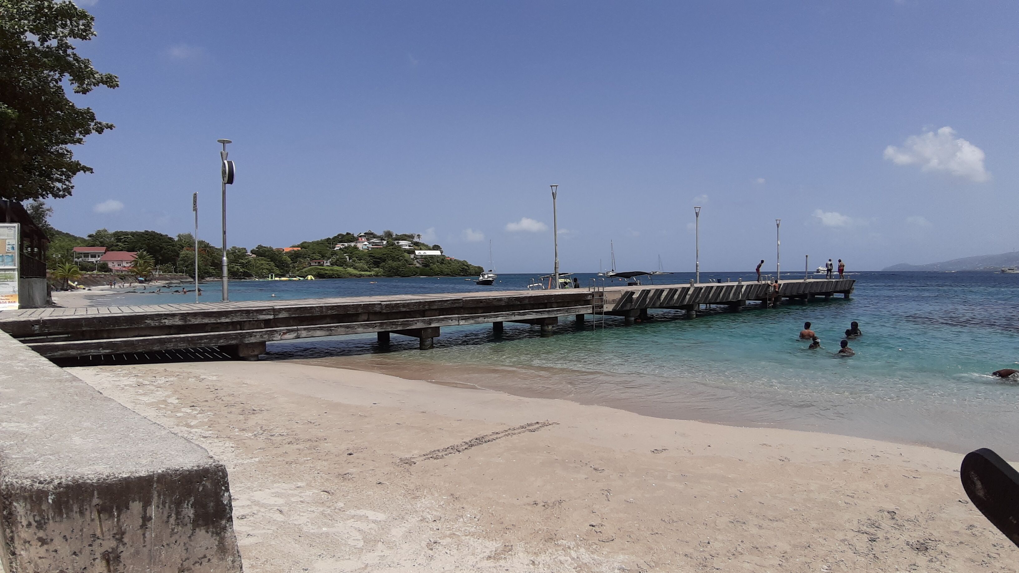 A beach with a pier extending into the water, clear skies, and a few people swimming.