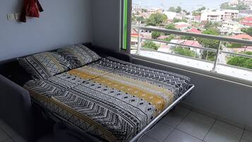A bedroom with a bed, a window with a view of a town, and a red curtain.