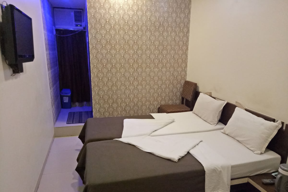 Ein Zimmer mit einem Bett, einem kleinen Tisch, einem Mülleimer und einem an der Wand befestigten Fernseher.