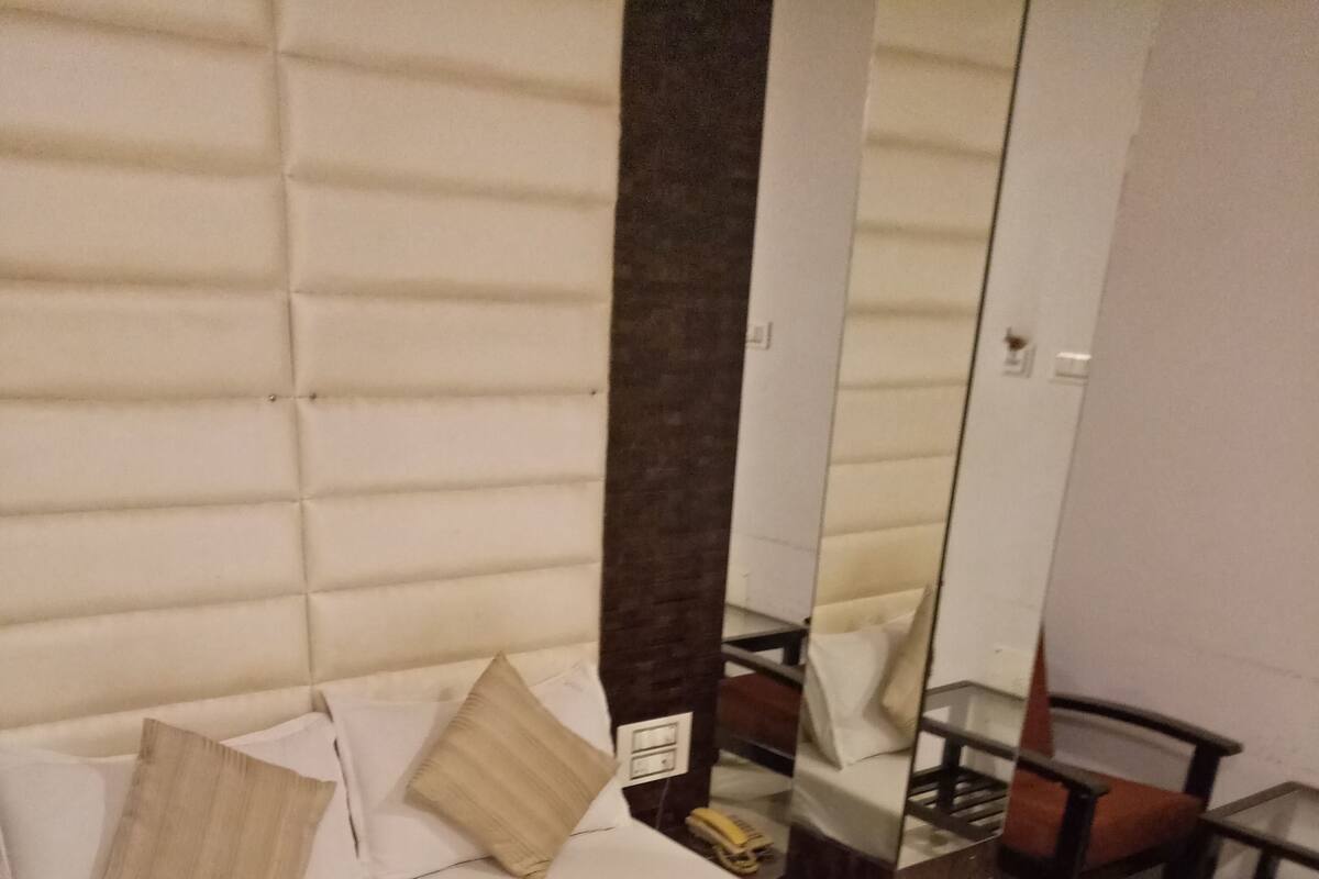 Ein ordentlich bezogenes Bett mit gestreiftem Bettwäsche und zwei Kissen, ein Nachttisch mit Telefon sowie ein Spiegel, der einen Teil des Raumes widerspiegelt.