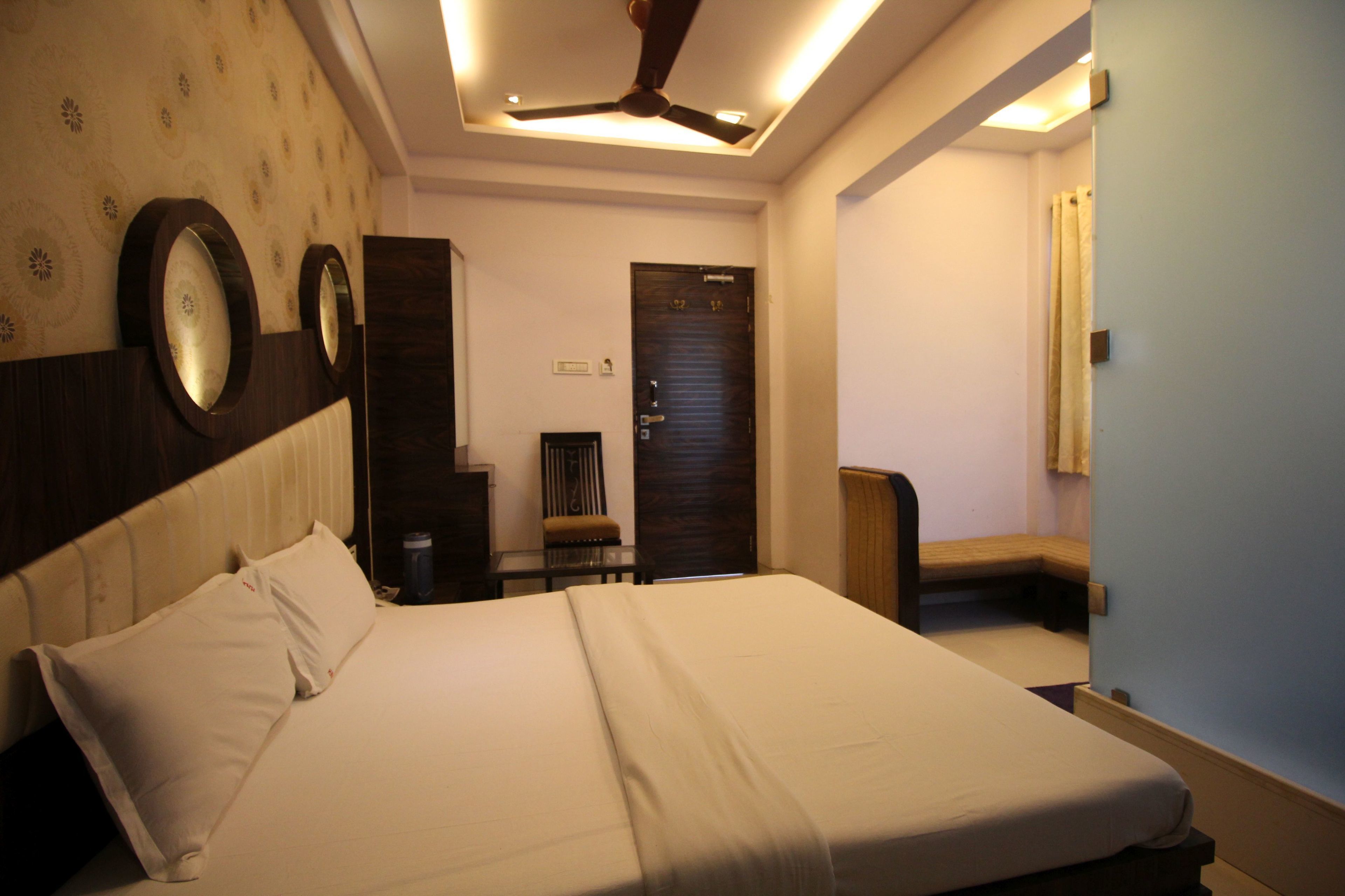 A hotel room with a large bed, a ceiling fan, a wooden wardrobe, a desk, and a chair.