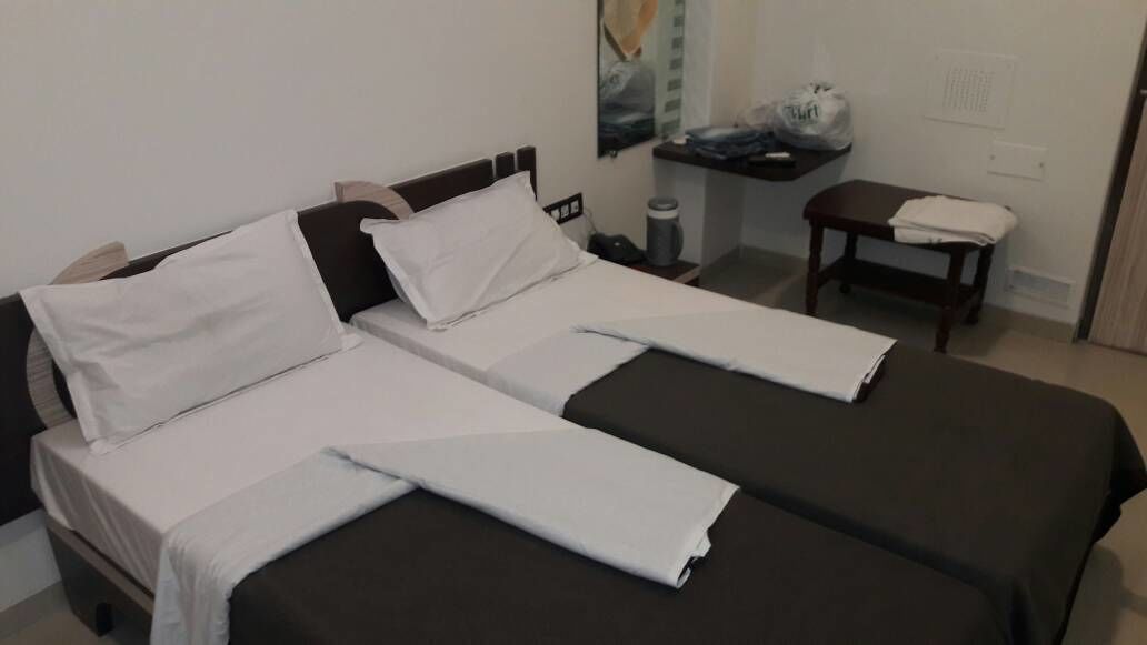 A double bed with white linens, a bedside table with a lamp, and a small nightstand with a trash can.