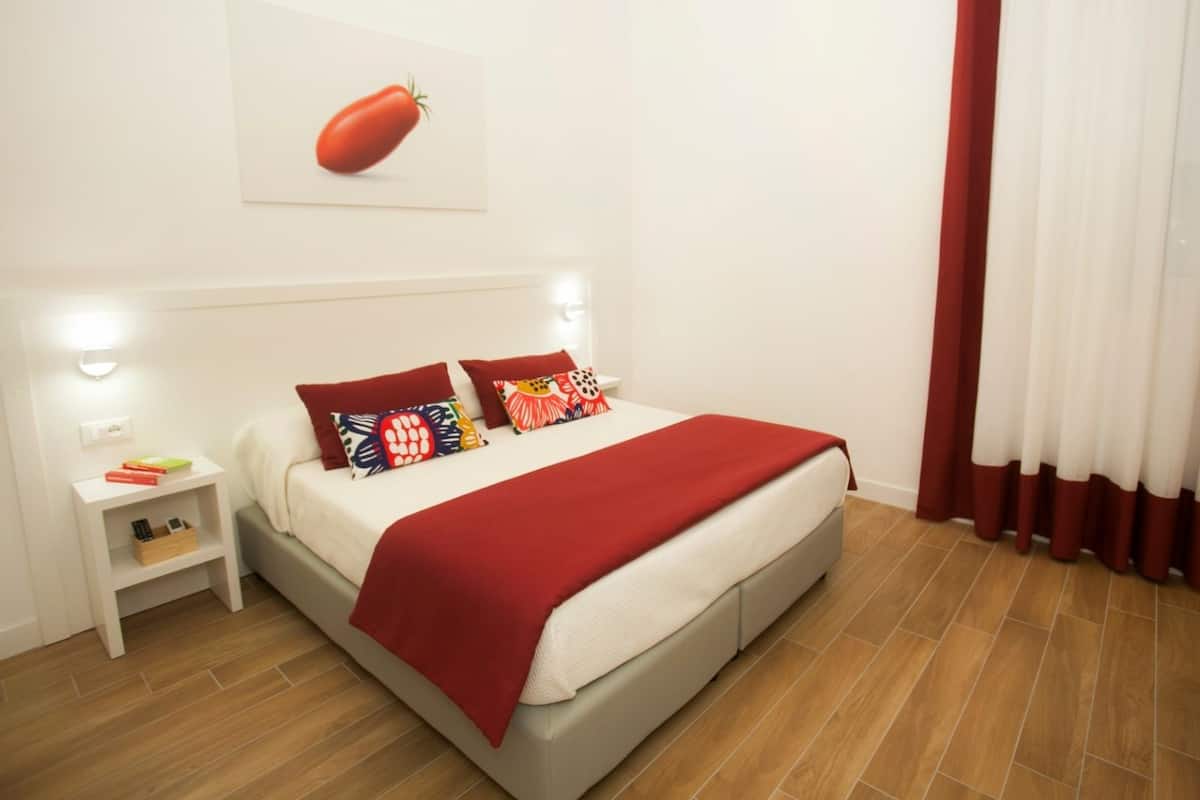 A neatly arranged bedroom with a bed, pillows, a nightstand, and a wall-mounted light.