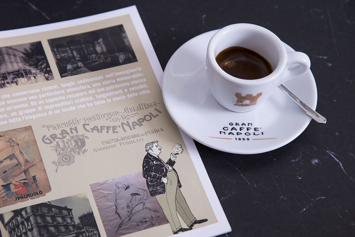 A cup of coffee on a saucer with a spoon, next to a menu with illustrations and text.