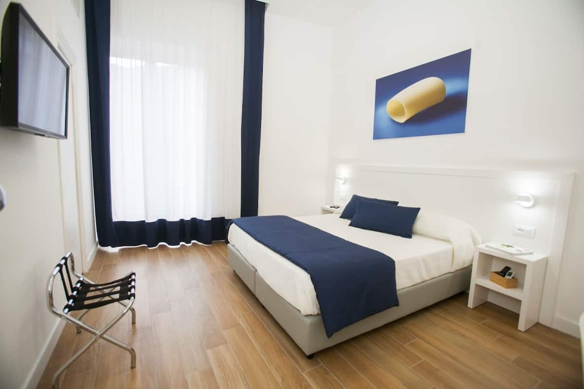 A hotel room with a bed, bedside tables, a chair, and a window with curtains.