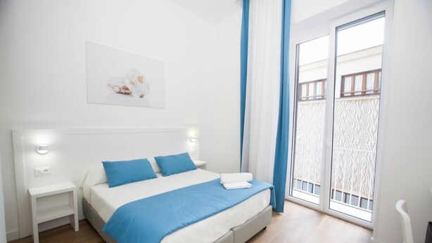 A modern bedroom with a bed, nightstands, and a view of a balcony. - Mediterranean Rooms (Castellammare di Stabia)