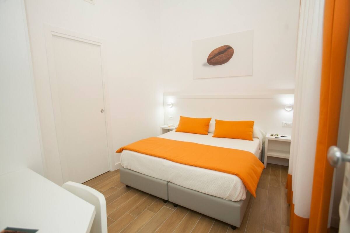 A bedroom with a bed, two nightstands, a desk, and a door.