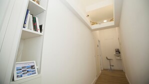 A narrow hallway with white walls, a wooden floor, and a small shelf with books and a digital photo frame. - Mediterranean Rooms (Castellammare di Stabia)