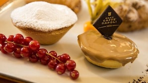 A dessert plate with a powdered pastry, a glazed donut, and a red currant garnish. - Mediterranean Rooms (Castellammare di Stabia)