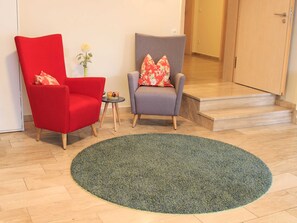 A room with two armchairs, one red and one grey, both with floral cushions, a small table with a vase of flowers, and a large green rug. - Double room large (without balcony) - Brewery-Gasthof Pfister (Eggolsheim)
