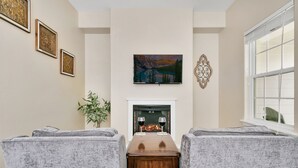 Ein Wohnzimmer mit Kamin, zwei Sesseln, einem Couchtisch und einem Gemälde an der Wand.
