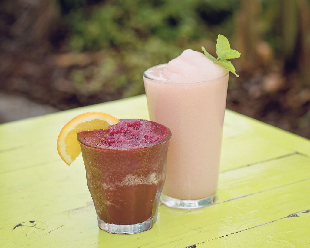 Two glasses of iced beverages on a yellow table with a blurred natural background.