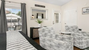 Una habitación con una cama, dos sillones con estampado, una mesita, un espejo y un cartel que dice "make today happy".