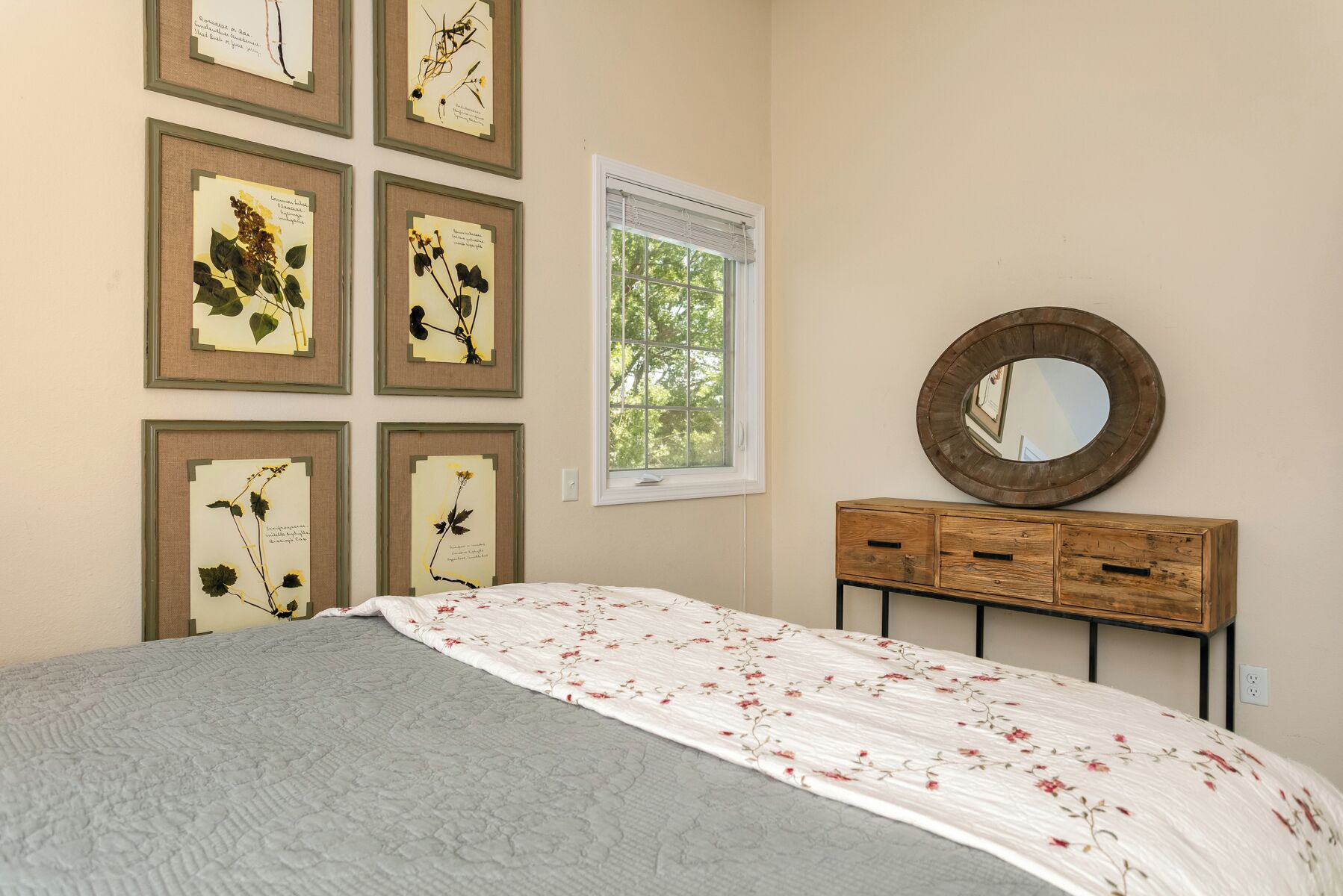 A bedroom with a bed, a dresser, a mirror, and framed botanical prints on the wall.