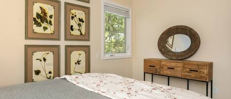 A bedroom with a bed, a dresser, a mirror, and framed botanical prints on the wall.
