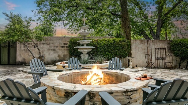 Un patio al aire libre con un hogar de piedra, rodeado de sillas Adirondack y una fuente de piedra decorativa.