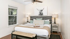A bedroom with a bed, bedside tables, a bench, a ceiling fan, and a window.