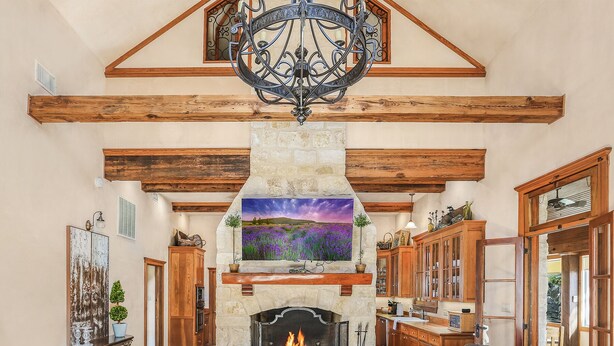 A cozy living room with a stone fireplace, wooden beams, and a chandelier.