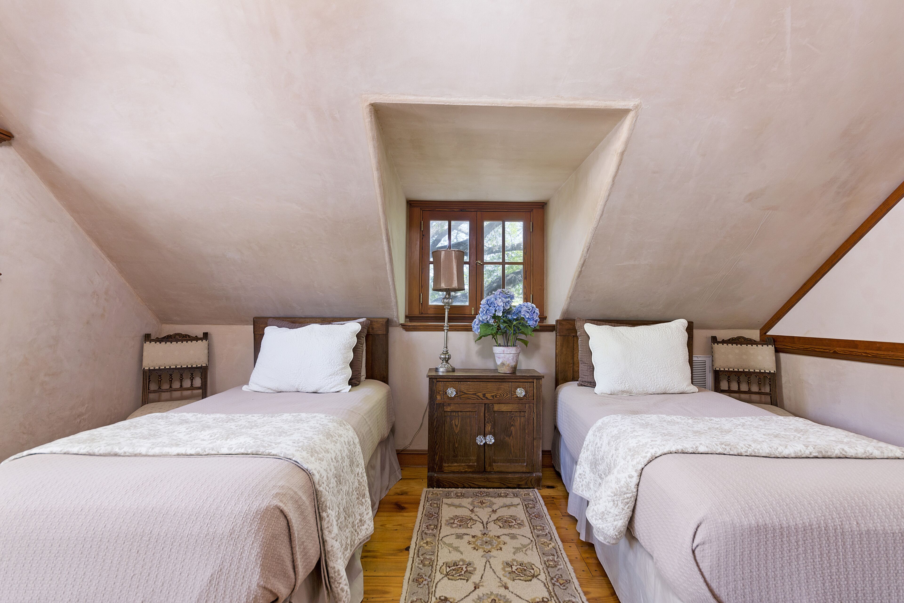 A bedroom with two beds, a wooden dresser, a window with a view, and a floral rug.