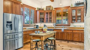 A kitchen with wooden cabinets, a stainless steel refrigerator, a wooden island with stools, and a window overlooking the yard.