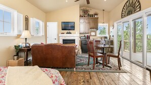 A spacious living area with a fireplace, a dining table with chairs, a sofa, and a large window offering a view of the outdoors. - Distant Views | Incredible Views | Gas Fireplace | Queen Bed (Fredericksburg)