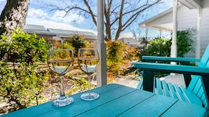 Twee wijnglazen op een blauwgroene tafel, met uitzicht op een overdekt terras en gebouwen op de achtergrond.