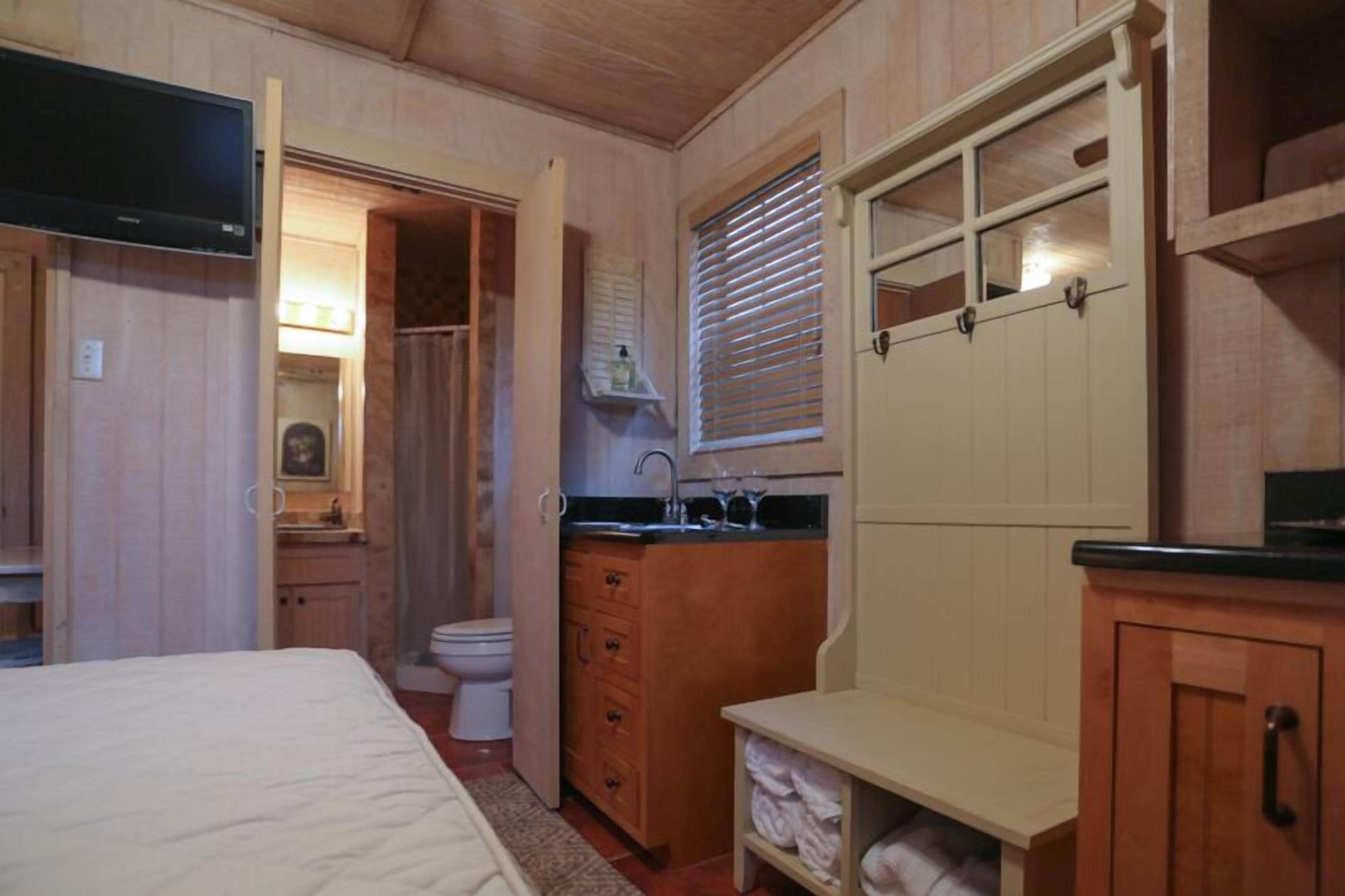 Una camera compatta con un letto, un bagno piccolo con il water e il lavandino, e un televisore montato a parete.