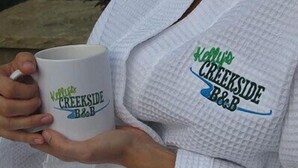 Una persona sostiene una taza blanca con el logo de 'Kerr's Creekside B&B'.