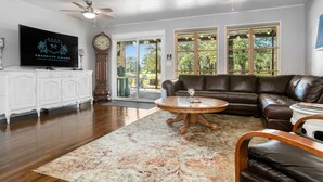 A spacious living room with a leather sofa, a coffee table, and a television on a white cabinet. - Harrys House | 3/2 Cottage | Full Kitchen | Hot Tub | In Town (Fredericksburg)