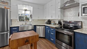 A modern kitchen with white cabinets, stainless steel appliances, and a wooden bench. - Harrys House | 3/2 Cottage | Full Kitchen | Hot Tub | In Town (Fredericksburg)