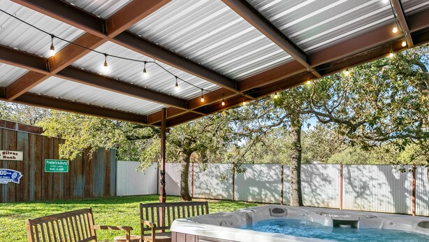 A covered outdoor patio with a hot tub, wooden benches, and string lights. - Harrys House | 3/2 Cottage | Full Kitchen | Hot Tub | In Town (Fredericksburg)