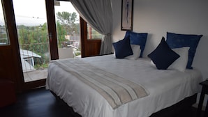 A bedroom with a large bed, a view through a window, and a balcony. - Oudtshoorn Homestay Accommodation (Oudtshoorn)